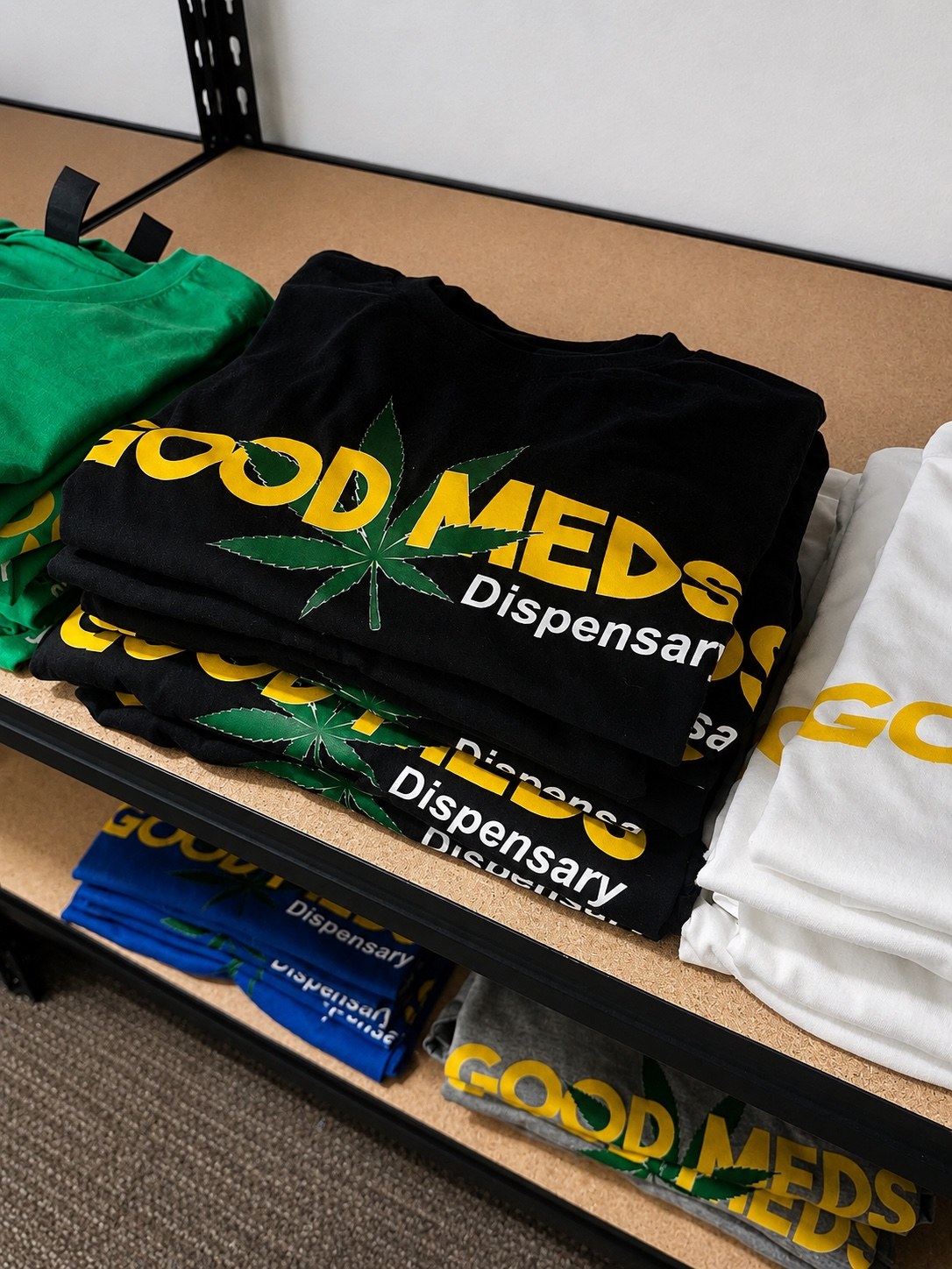 Good Meds logo T-shirts in black, green, white, blue, and gray on display in the store